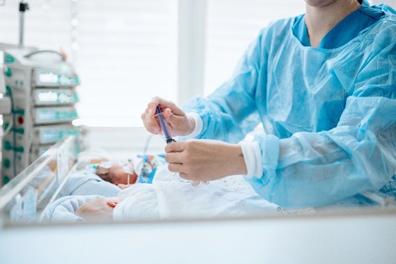 Pflegefachkraft beugt sich über das Bettchen von zwei Neugeborenen und versorgt sie.