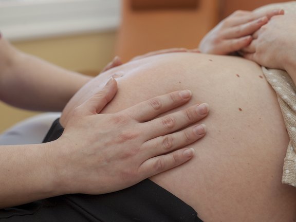 Hebamme tastet Bauch der werdenden Mutter ab.