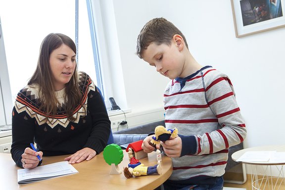 Eine Psychologin unterhält sich mit einem Jungen, der mit Spielzeugfiguren spielt.