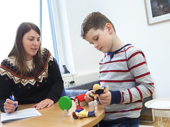 Eine Psychologin unterhält sich mit einem Jungen, der mit Spielzeugfiguren spielt.