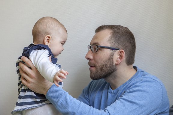Ein junger Vater hält sein Baby hoch und blickt ihm in die Augen.