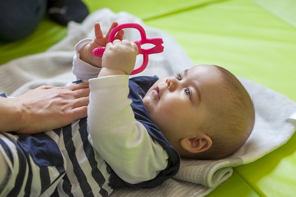 Ein Baby liegt auf einer Decke und spielt.