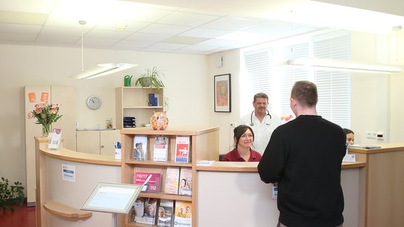 Urologe Agim Ismani, Medizinische Fachangestellte und ein Patient am Empfangstresen der Praxis.