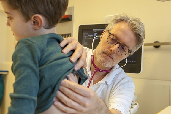 Chefarzt Dr. med. Georg Hillebrand horcht einen kleinen Patienten mit dem Stetoskop ab.