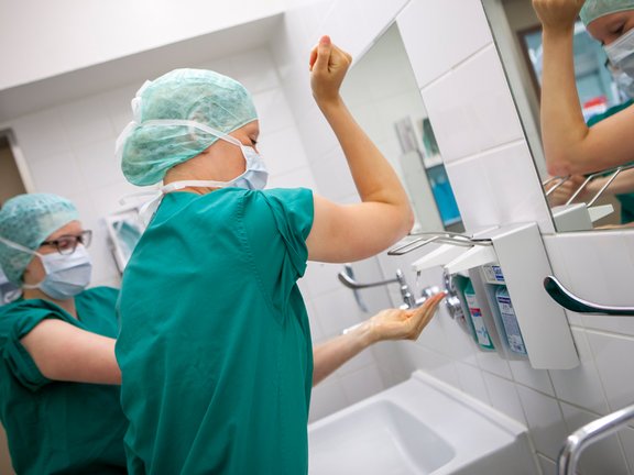 Zwei medizinische Fachkräfte bereiten sich auf eine OP vor und desinfizieren sich Hände und Arme