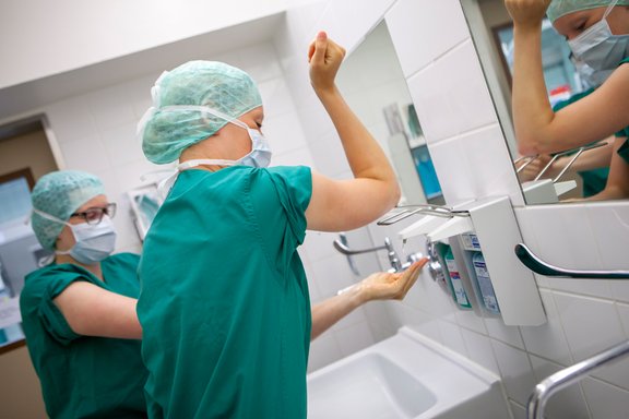 Zwei medizinische Fachkräfte bereiten sich auf eine OP vor und desinfizieren sich Hände und Arme