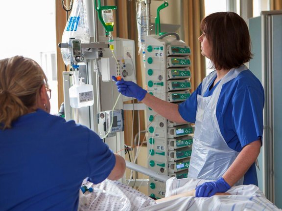 Eine Mitarbeiterin kontrolliert die Überwachungsgeräte, eine Mitarbeiterin kümmert sich um der/dem PatientIn