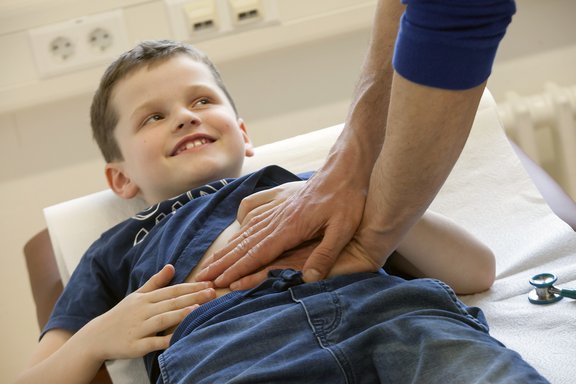 Ein Junge liegt auf einer Untersuchungsliege während ein Mediziner seinen Bauch abtastet.