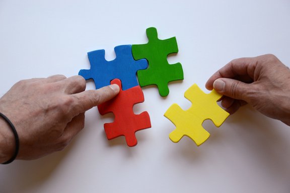 Es sind zwei Hände und vier bunte Puzzleteile abgebildet