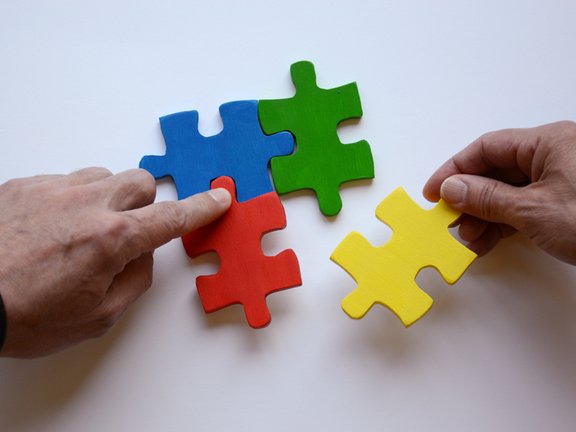 Es sind zwei Hände und vier bunte Puzzleteile abgebildet