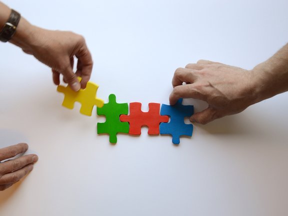 Es sind drei Hände und vier bunte Puzzleteile abgebildet