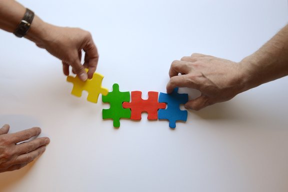 Es sind drei Hände und vier bunte Puzzleteile abgebildet