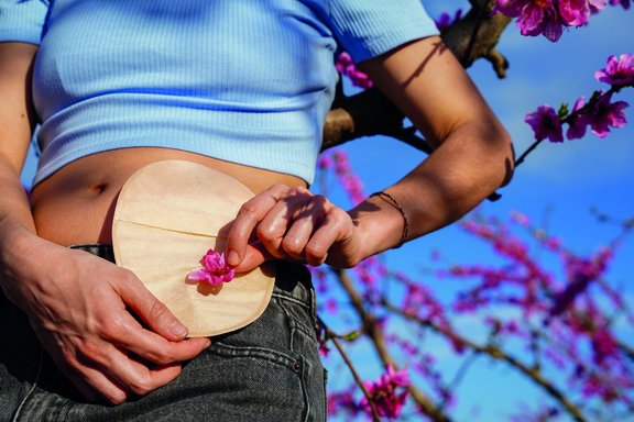Person hält eine runde Scheibe mit einer Blüte vor dem Bauch als Symbol für das Leben mit einem Stoma