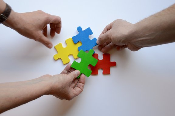 Es sind drei Hände und vier bunte Puzzleteile abgebildet