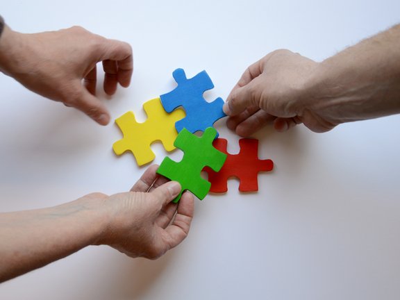 Es sind drei Hände und vier bunte Puzzleteile abgebildet