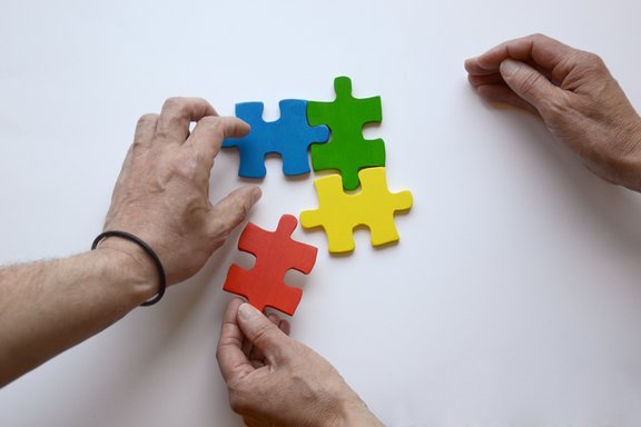 Es sind zwei Hände und vier bunte Puzzleteile abgebildet
