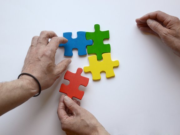 Es sind zwei Hände und vier bunte Puzzleteile abgebildet