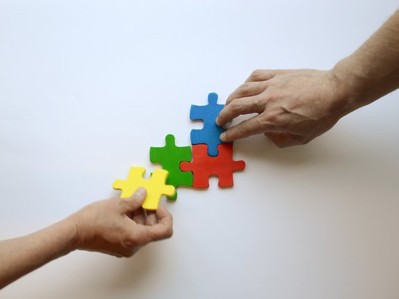 Es sind zwei Hände und vier bunte Puzzleteile abgebildet