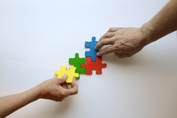 Es sind zwei Hände und vier bunte Puzzleteile abgebildet