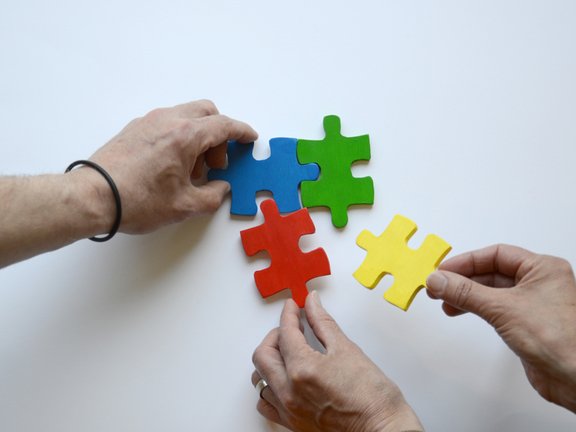 Es sind drei Hände und vier bunte Puzzleteile abgebildet