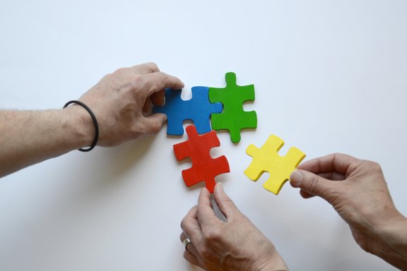 Es sind drei Hände und vier bunte Puzzleteile abgebildet