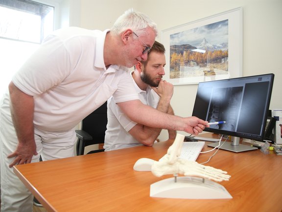 Neurochirurg Jens Mechler und Orthopäde Dr. Maximilian Justus Heintzen schauen sich ein Röntgenbild an, im Vordergrund ein Fußskelett.