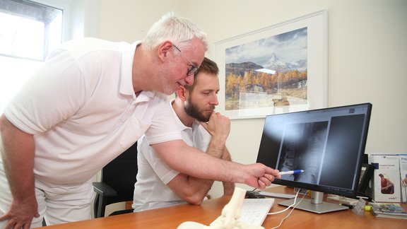 Neurochirurg Jens Mechler und Orthopäde Dr. Maximilian Justus Heintzen schauen sich ein Röntgenbild an, im Vordergrund ein Fußskelett.