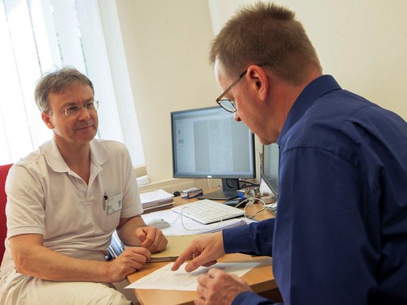 Arzt sitzt mit einem Patienten am Tisch und erklärt die Behandlungsmethode