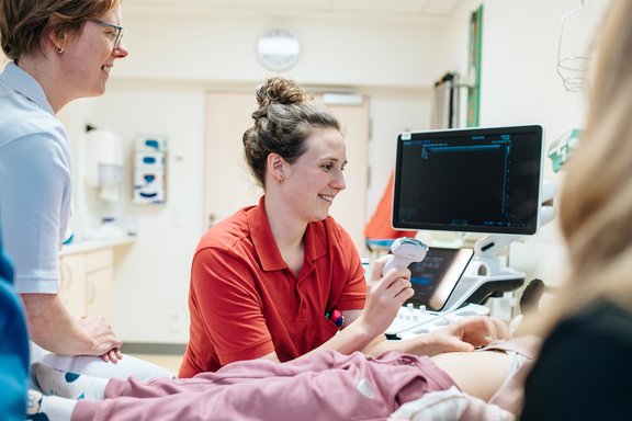 Ärztin und Pflegefachkraft sitzen am Bett eines Kindes und machen eine Sonografie.