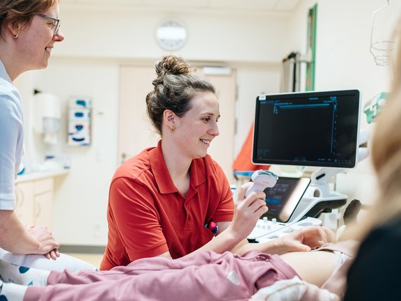 Ärztin und Pflegefachkraft sitzen am Bett eines Kindes und machen eine Sonografie.