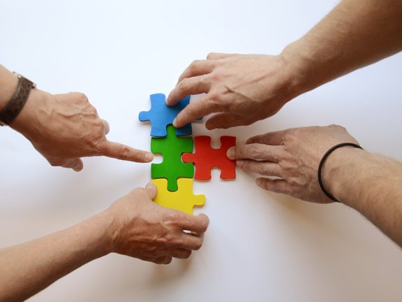 Es sind vier Hände und vier bunte Puzzleteile abgebildet