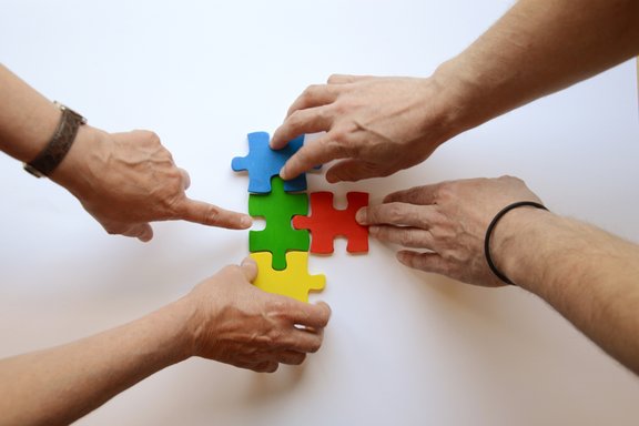 Es sind vier Hände und vier bunte Puzzleteile abgebildet