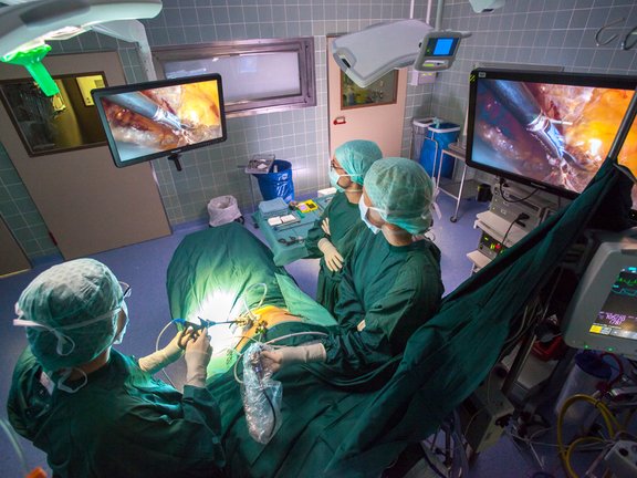 Minimalinvasive Operation im OP-Saal, drei medizinische Fachkärfte stehen am OP-Tisch und blicken auf den OP-Monitor