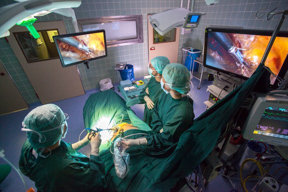 Minimalinvasive Operation im OP-Saal, drei medizinische Fachkärfte stehen am OP-Tisch und blicken auf den OP-Monitor