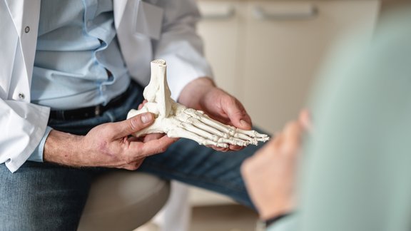Arzt hält ein Fußskelett in der Hand und erklärt