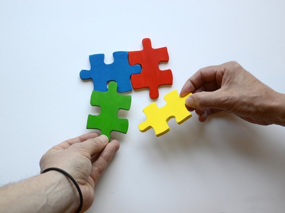 Es sind zwei Hände und vier bunte Puzzleteile abgebildet