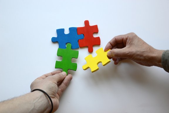 Es sind zwei Hände und vier bunte Puzzleteile abgebildet