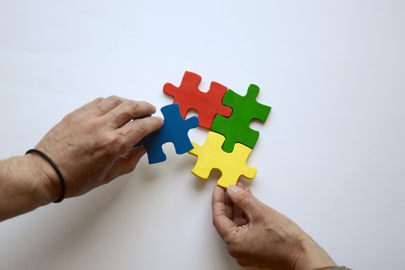 Es sind zwei Hände und vier bunte Puzzleteile abgebildet