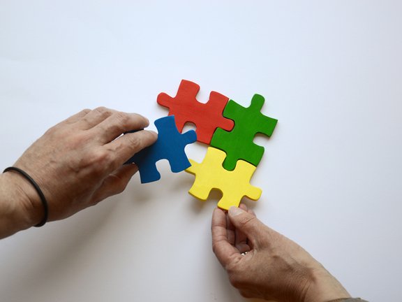 Es sind zwei Hände und vier bunte Puzzleteile abgebildet
